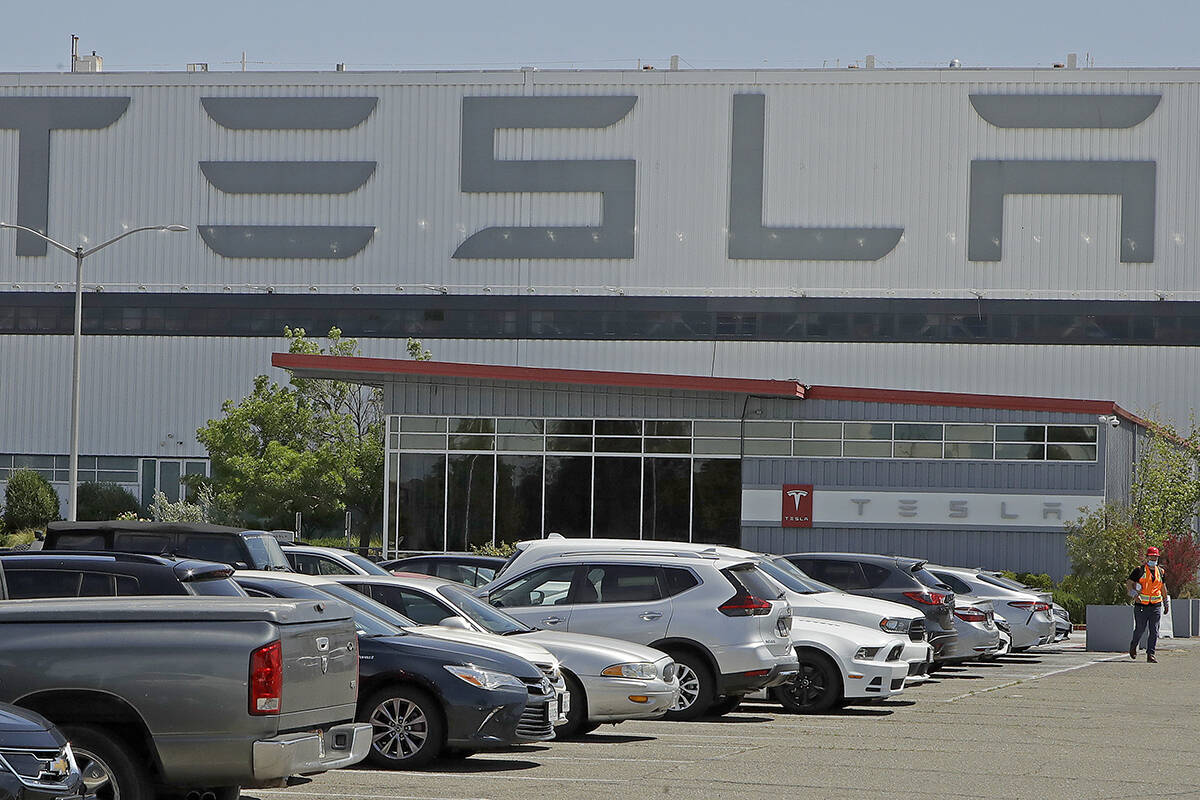 FILE - A man walks in the Tesla plant parking lot, May 11, 2020, in Fremont, Calif. Factory wor ...