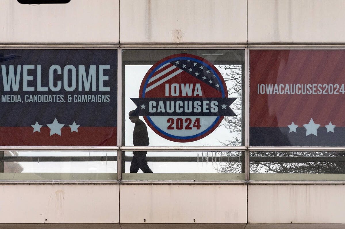 A man walks past a sign that reads "Iowa Caucuses 2024" in downtown Des Moines, Iowa, ...