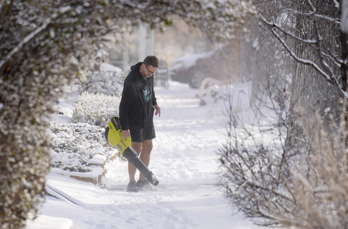 With the daytime high temperature far below zero, a man uses a leaf blower to clear a light sno ...