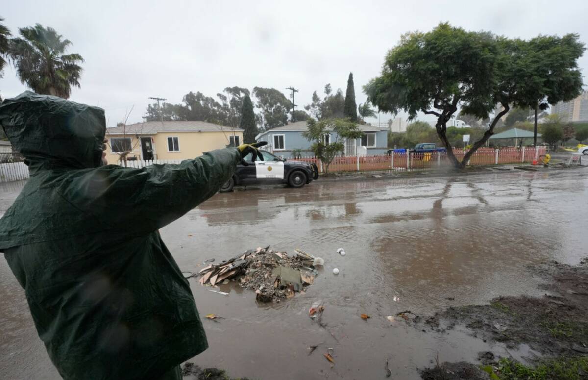 Ruben Gomez points along a partially flooded street as he breaks from clearing away mud and flo ...