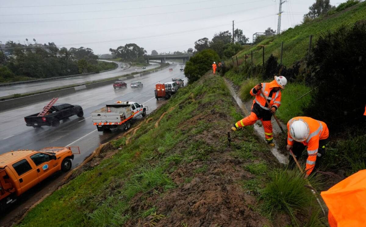 Workers clear debris from a canal to keep a hillside from flooding during a rain storm Thursday ...