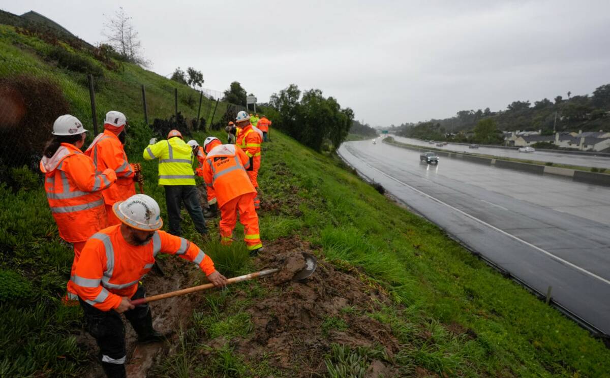 Workers clear debris from a canal to keep a hillside from flooding during a rain storm Thursday ...