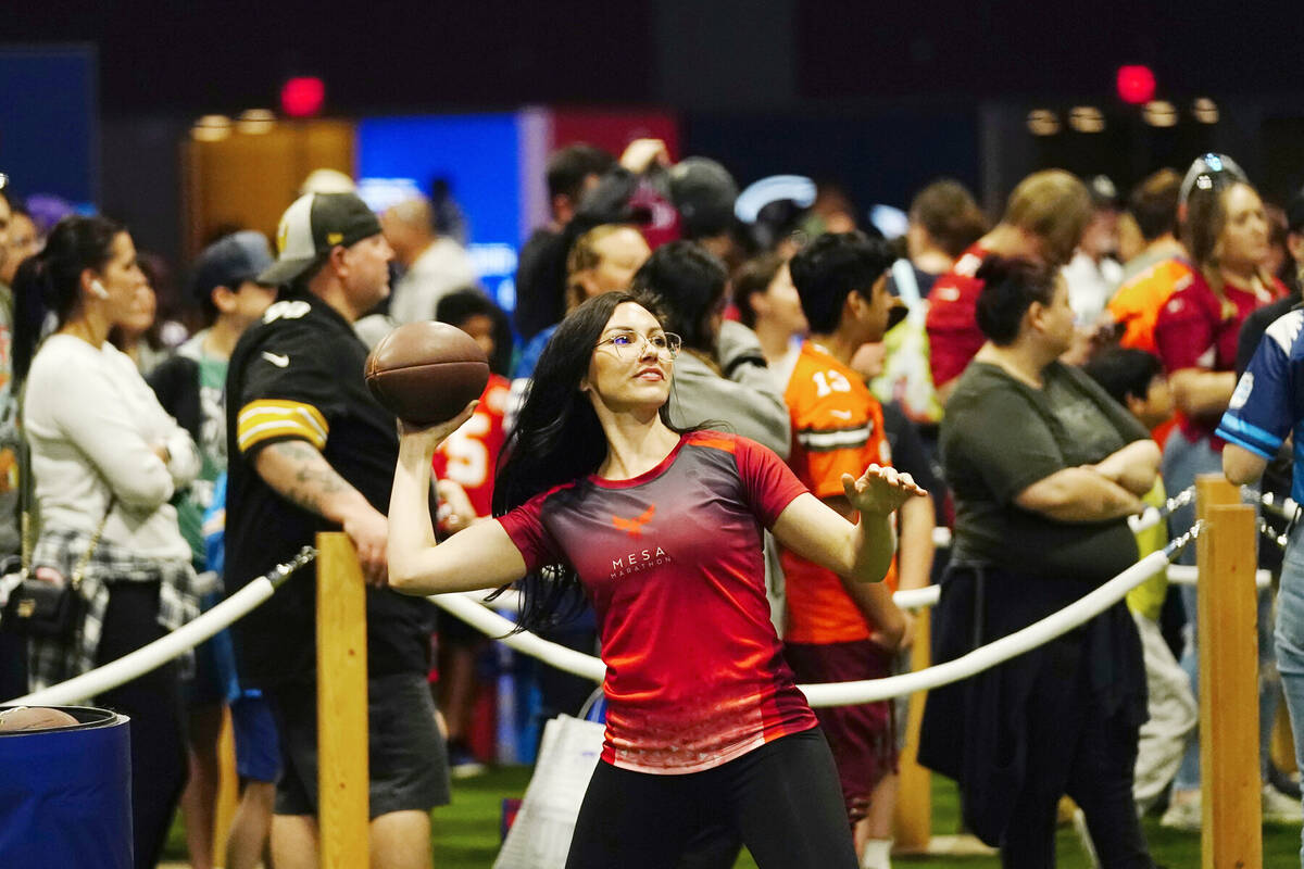 A participant throws a football in a passing exhibit at the Super Bowl Experience, the opening ...