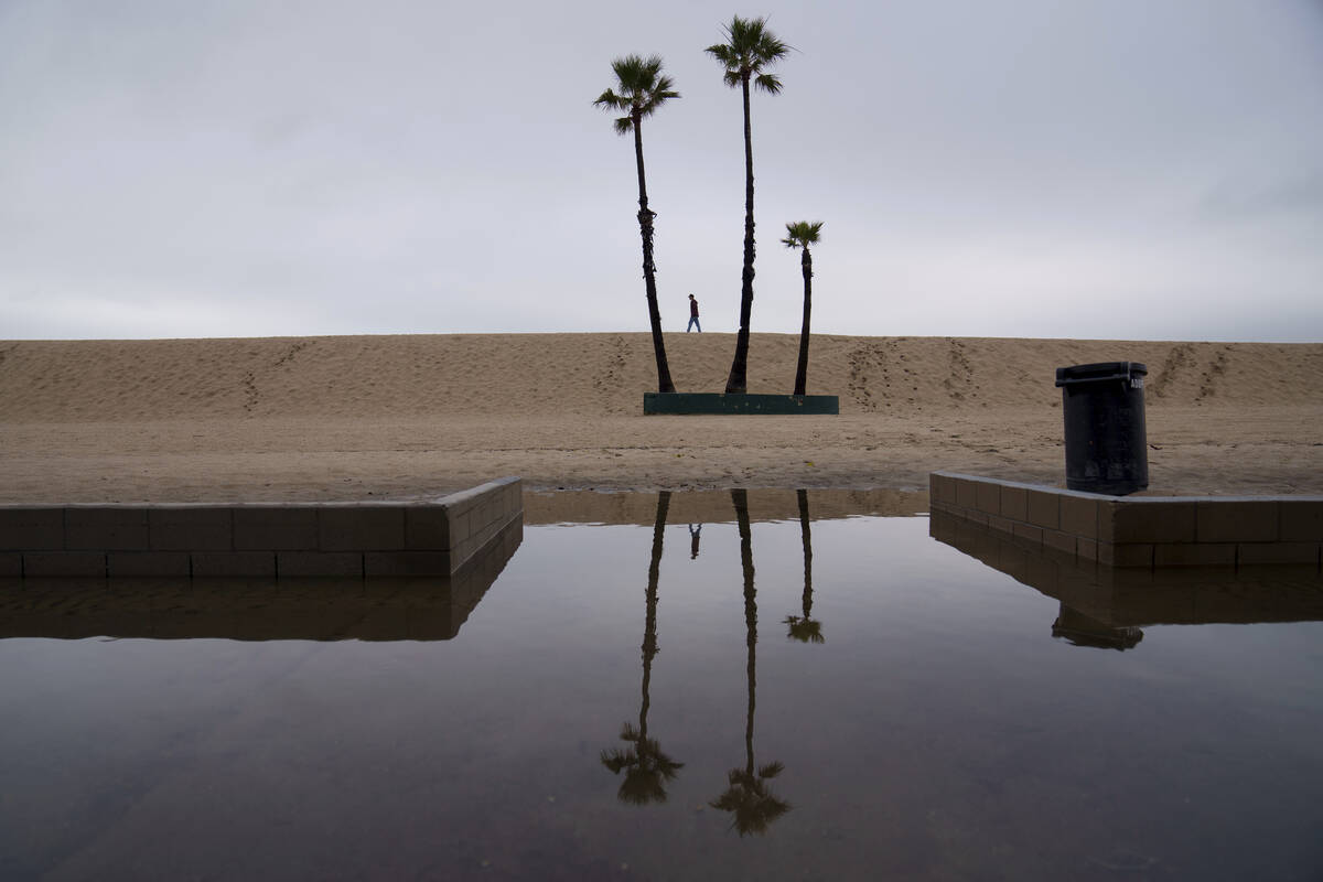 A person walks along the beach with flooding along the boardwalk Thursday, Feb. 1, 2024 in Seal ...