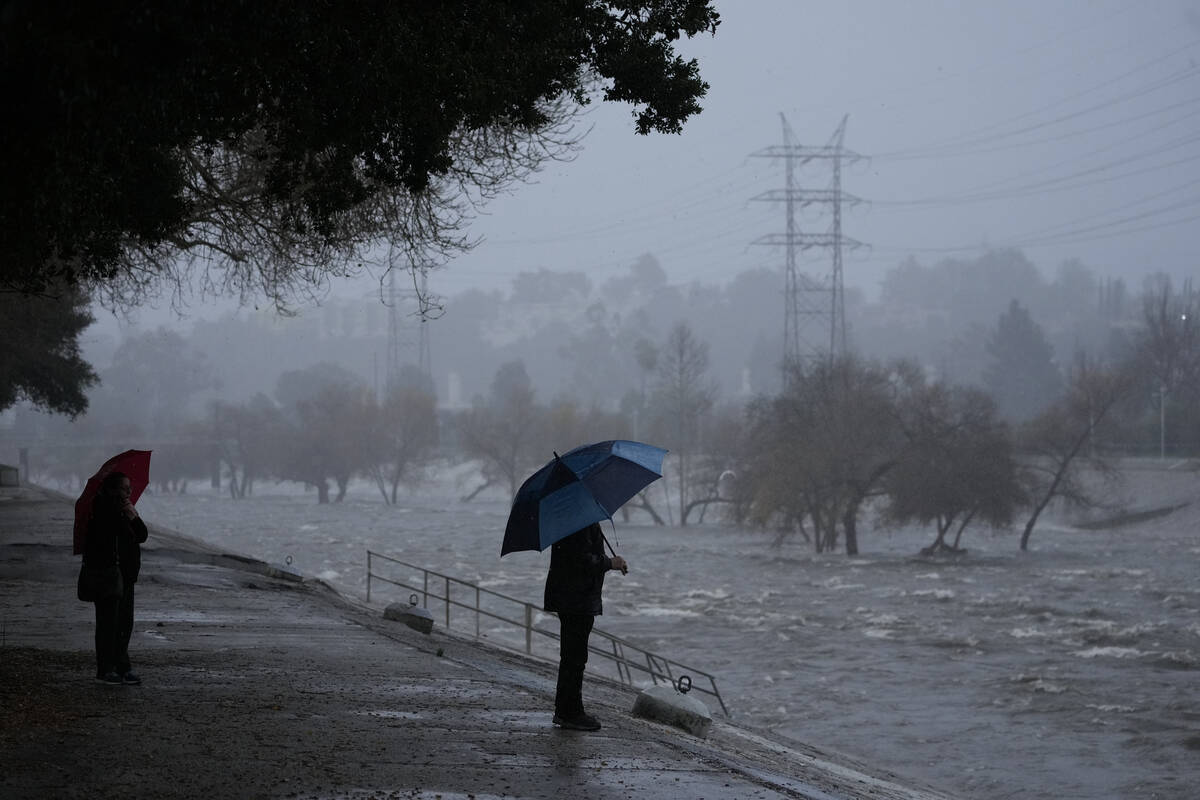 A couple walks on the edge of the Los Angeles River, carrying stormwater downstream Sunday, Feb ...