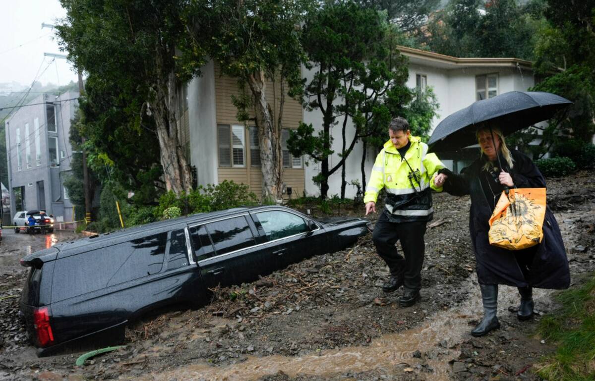 A first responder helps a resident evacuate from a neighborhood after a mudslide, Monday, Feb. ...