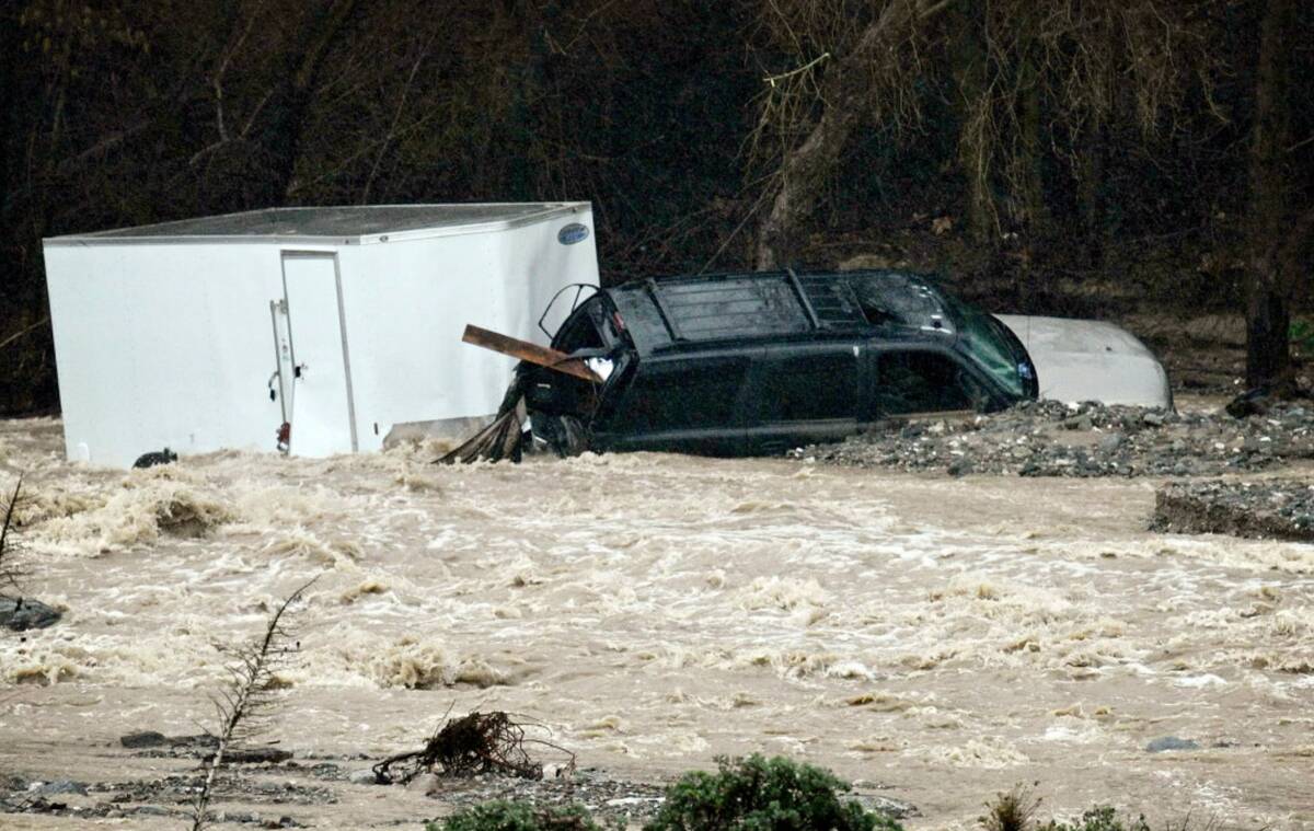 An SUV towing a trailer lies in the rocks on the bank of Cajon Creek near Devore, Calif., on Mo ...