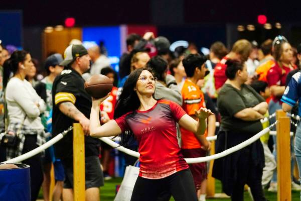 A participant throws a football in a passing exhibit at the Super Bowl Experience, the opening ...