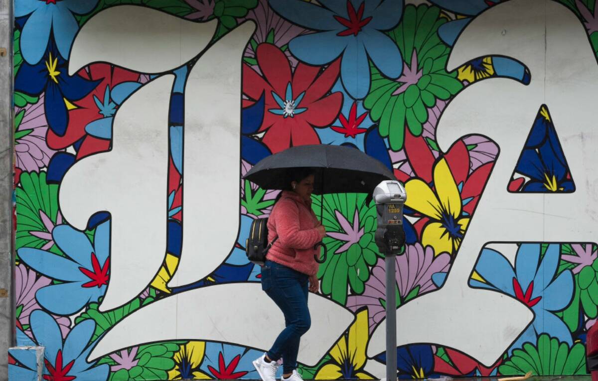 A woman walk under the rain in Los Angeles, Monday, Feb. 19, 2024. (AP Photo/Damian Dovarganes)