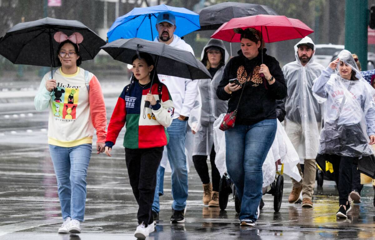 People walk with umbrellas and ponchos in the resort district near Disneyland in Anaheim, Calif ...