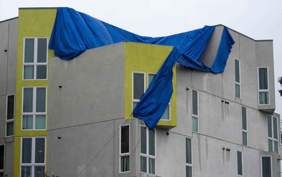 An apartment building roof is covered with a plastic tarp under heavy rain in Los Angeles, Mond ...