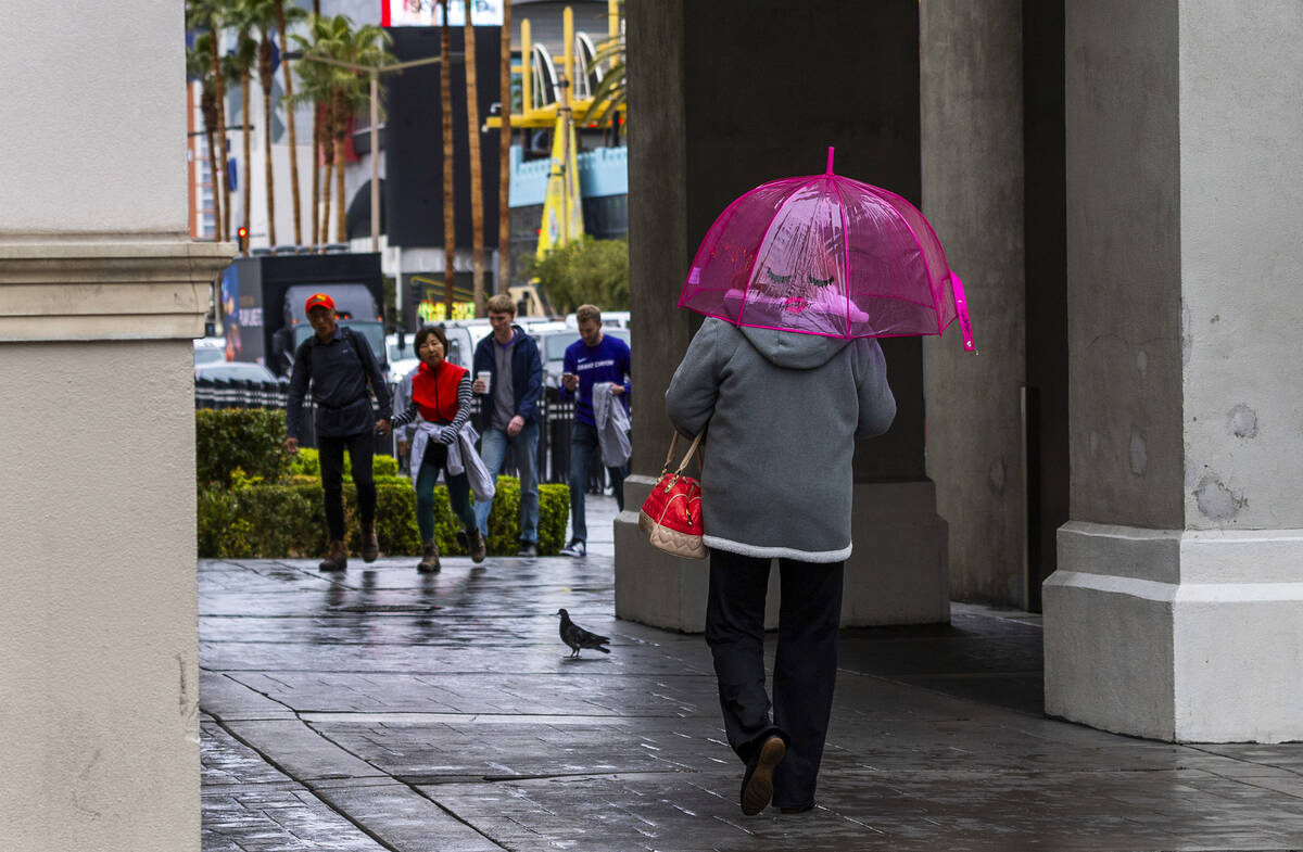 A woman walks with a fun umbrella along the Stripo near Caesars Palace during a rainy day on Fr ...