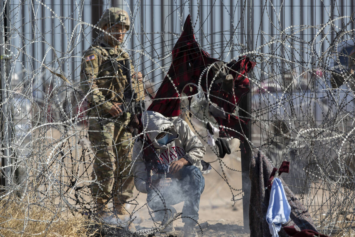 Male migrants are escorted south behind a barrier by the Texas National Guard on the Rio Grande ...