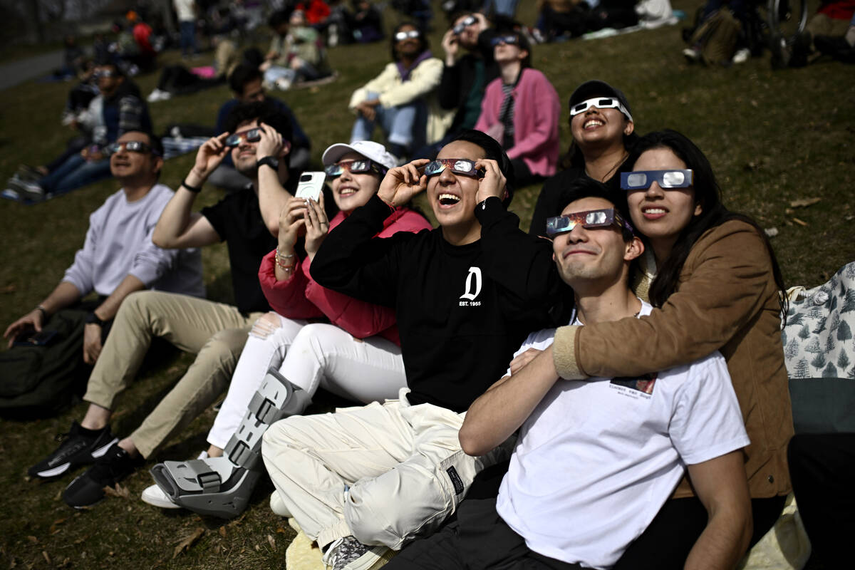 People wear solar eclipse glasses as they observe the partial phase of a total solar eclipse, i ...