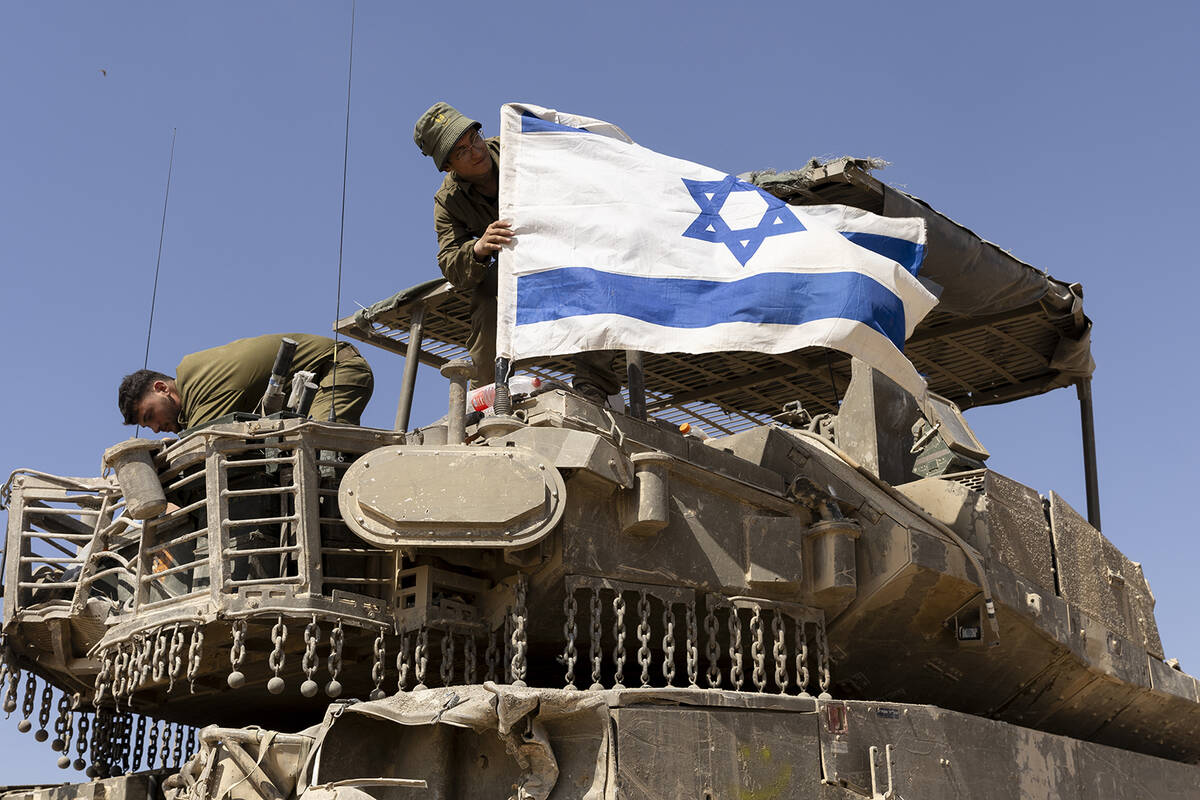 An Israeli soldier hangs an Israeli flag on an armored personnel carrier move near the border w ...