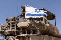 An Israeli soldier hangs an Israeli flag on an armored personnel carrier move near the border w ...