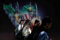 Iranian women without wearing their mandatory Islamic headscarf walk past a banner showing miss ...