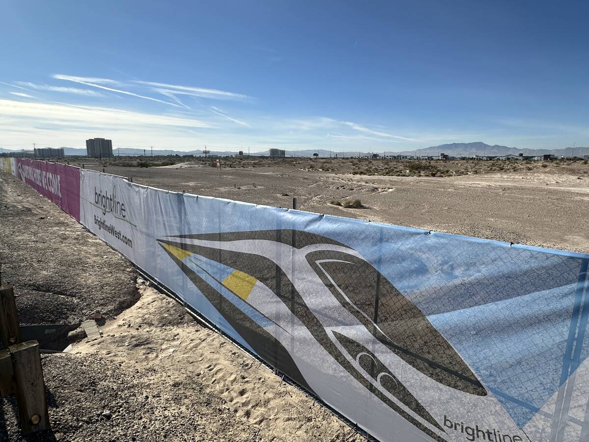 A fence with Brightline West imagery sits on a plot of land where the Las Vegas station of the ...