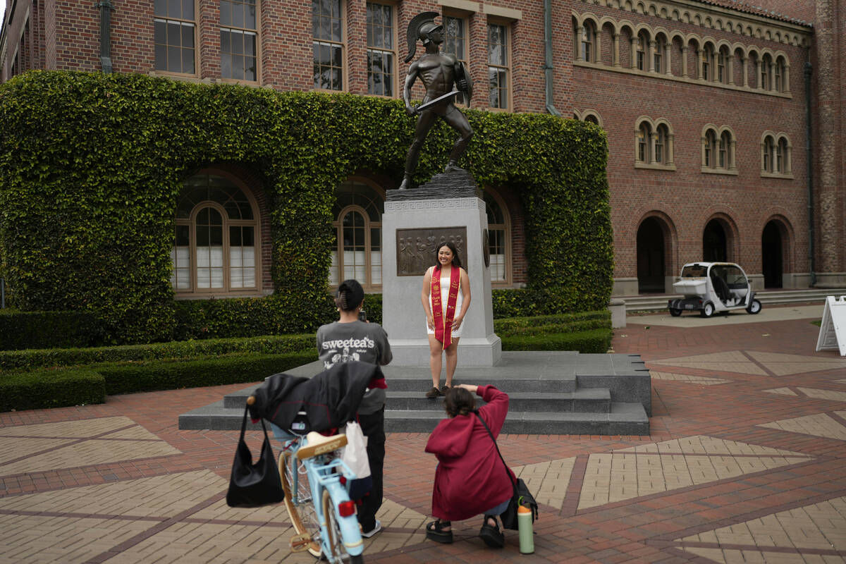 A graduating senior takes photos under the University of Southern California mascot on campus, ...
