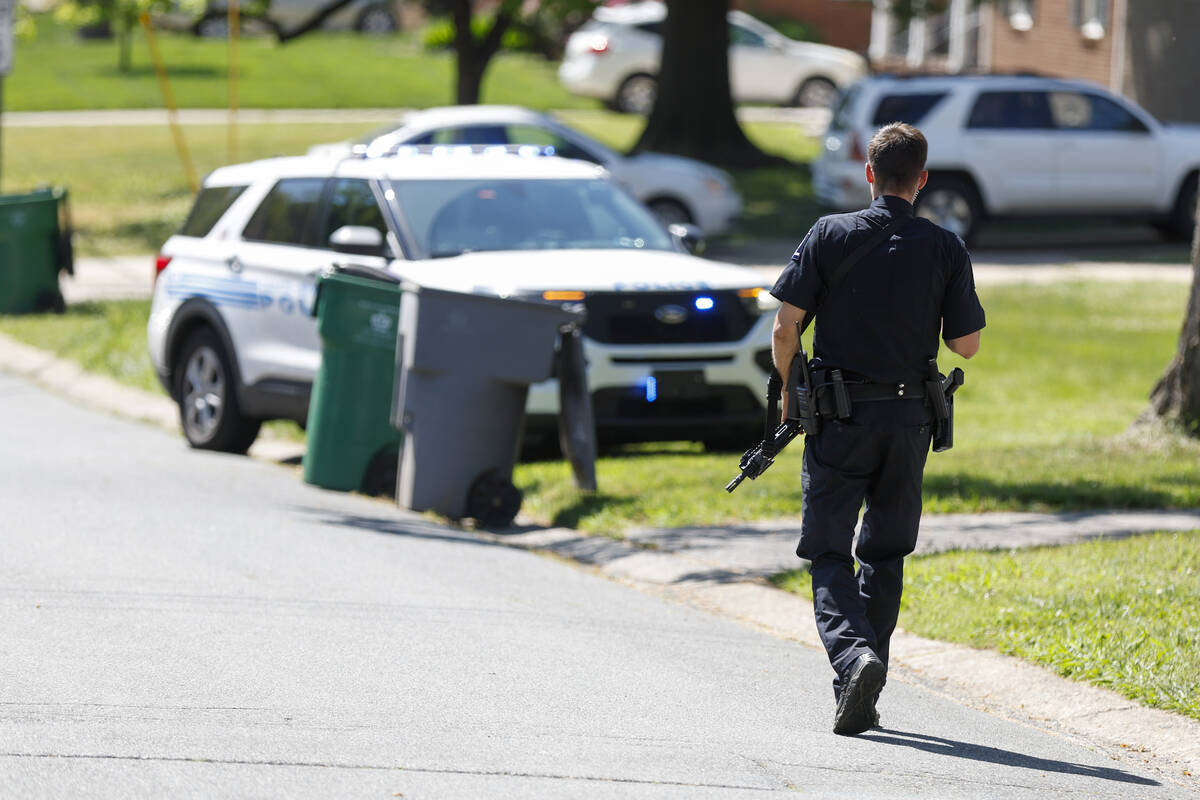 A Charlotte-Mecklenburg Police Department officer walks carrying a gun in the neighborhood wher ...