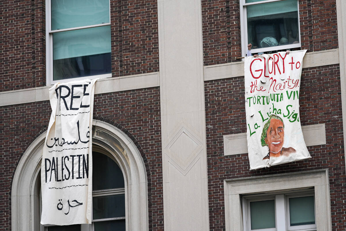 A demonstrator pumps his fist as he hangs a sign from a window in Hamilton Hall inside the Colu ...