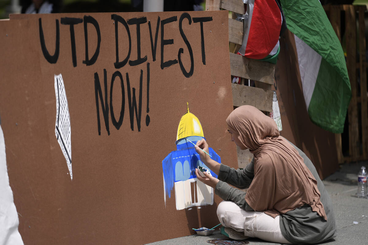 A woman paints on a barrier during a protest set up in a plaza at the University of Texas at Da ...
