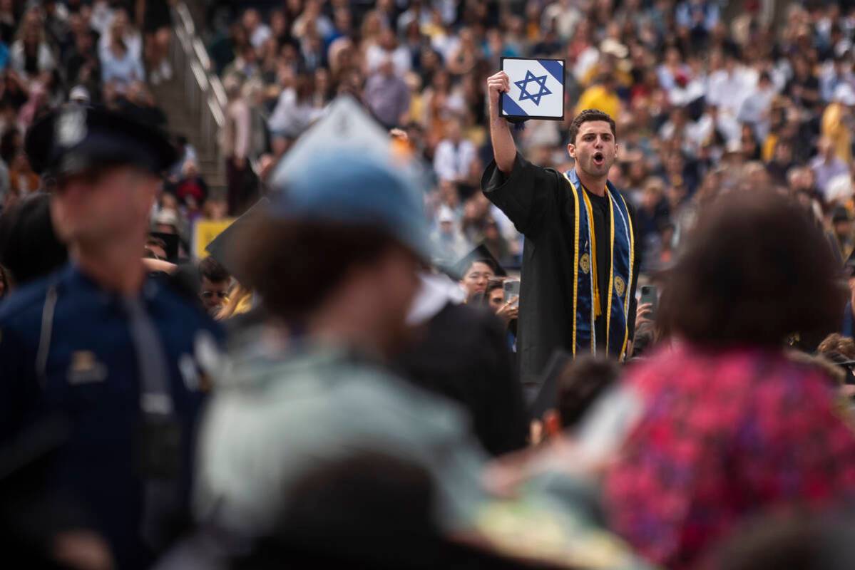 A graduate holds his cap with an Israeli flag while shouting at pro-Palestinian protesters as t ...