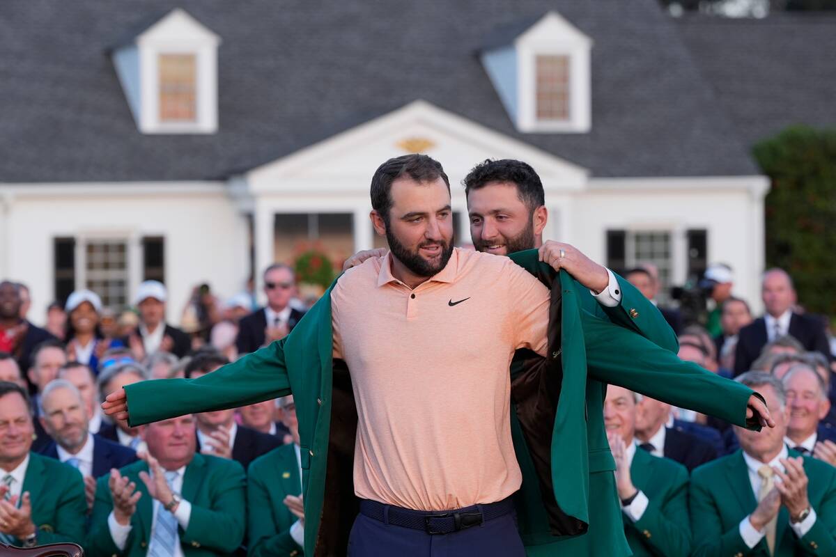 Jon Rahm, of Spain, puts the green jacket on winner Scottie Scheffler after the Masters golf to ...