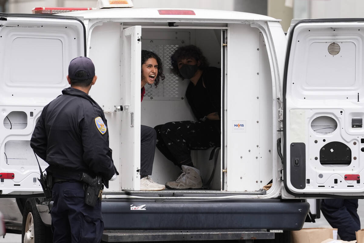A pro-Palestinian demonstrator shouts as she is detained in a police vehicle outside a building ...