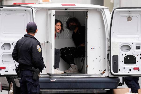 A pro-Palestinian demonstrator shouts as she is detained in a police vehicle outside a building ...