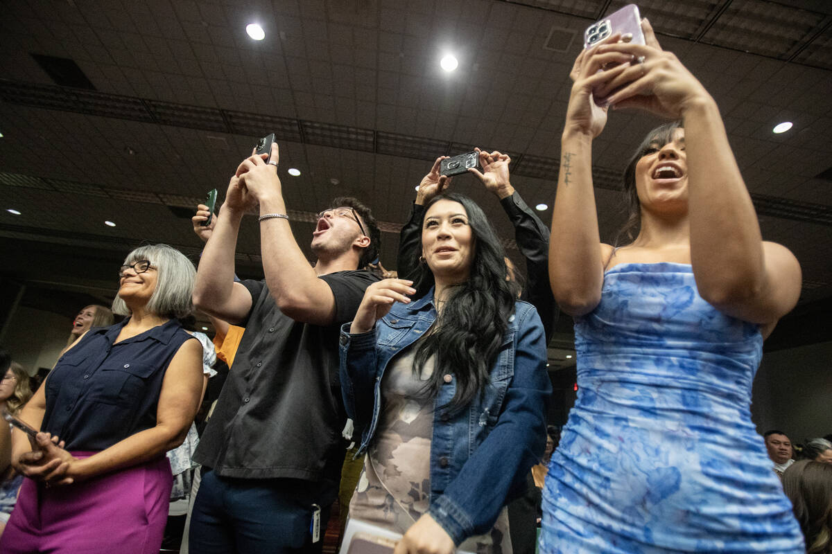 Friends and families cheer and wait to take photographs of graduates as they receive their badg ...