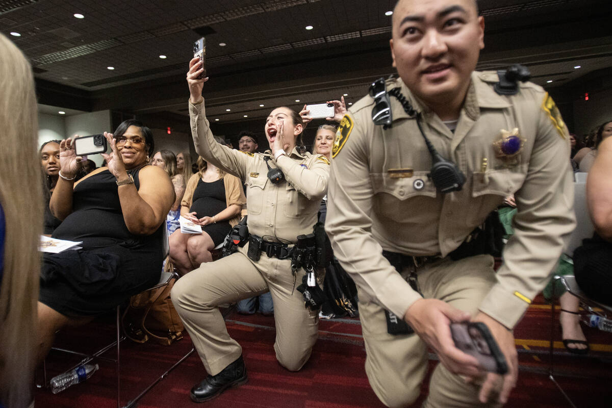 Friends and families cheer and wait to take photographs of graduates as they receive their badg ...