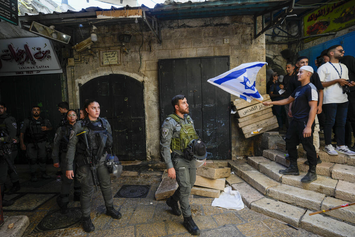 Israeli border police officers look at an Israeli as he waves a national flag during a march ma ...