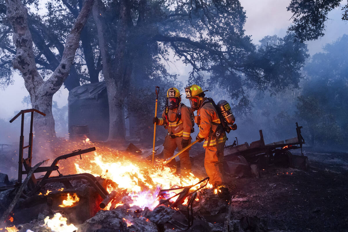 Firefighters extinguish a burning outbuilding as the Point Fire spreads along West Dry Creek Rd ...