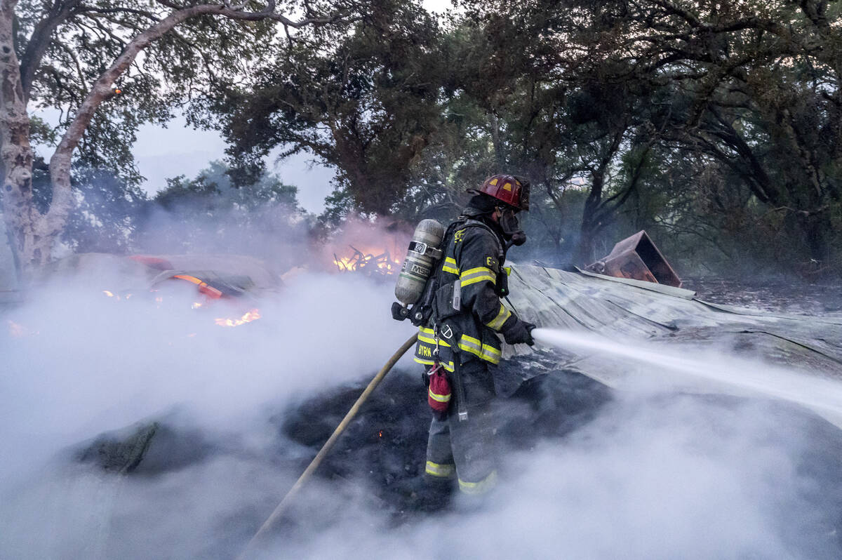A firefighter sprays water on a burning outbuilding as the Point Fire spreads along West Dry Cr ...