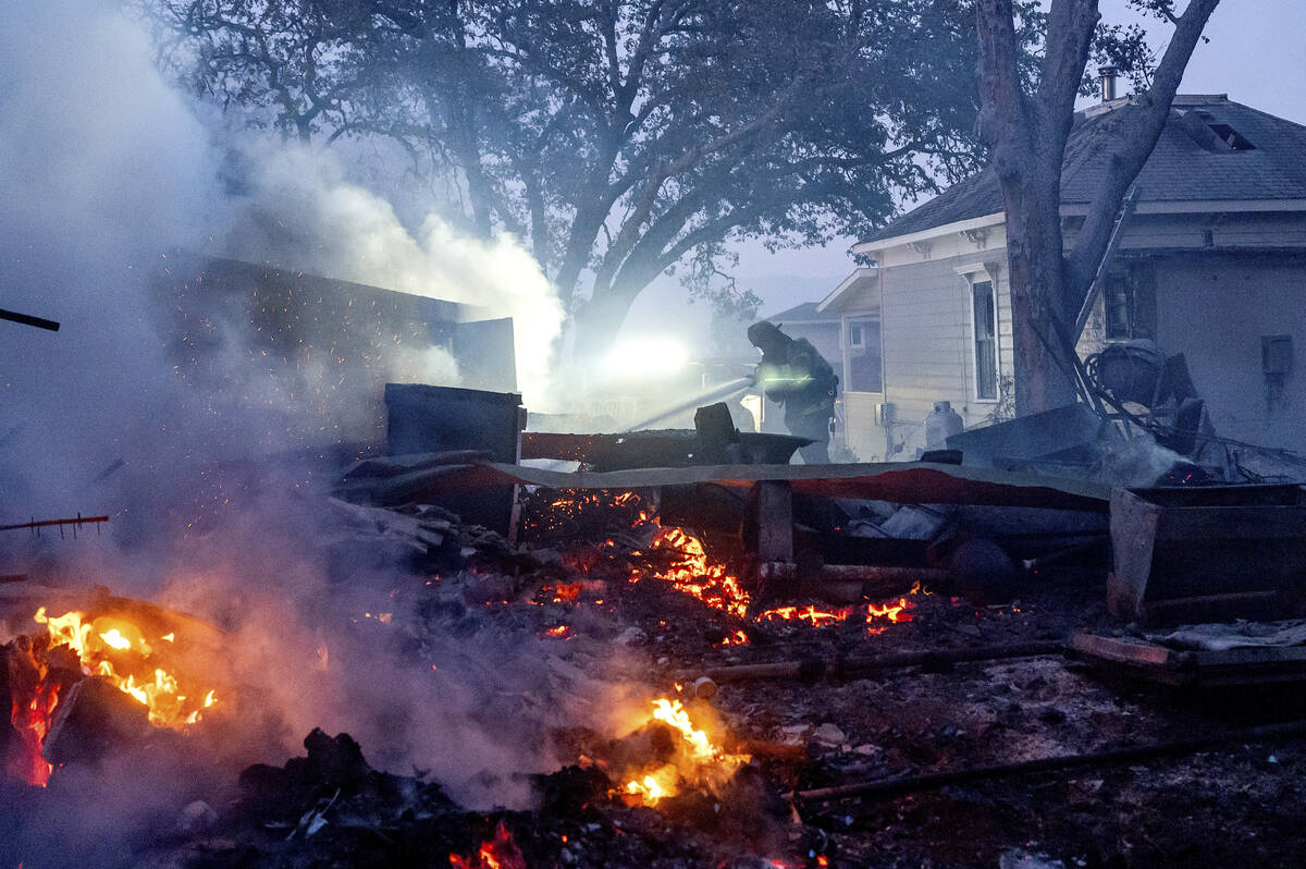 A firefighter sprays water on a burning outbuilding as the Point Fire spreads along West Dry Cr ...