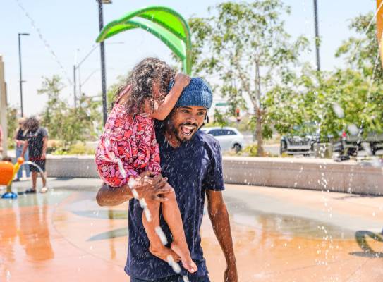 Danele Egzi takes his daughter Aya Egzi, 4, through the water feature at the splash pad at Trig ...