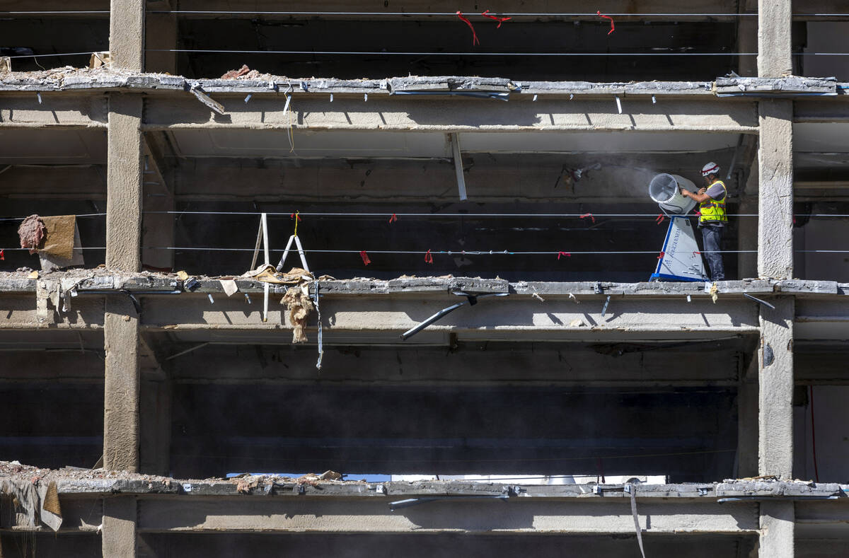 A construction worker adjusts a fog cannon keeping moisture on debris as it falls from above wh ...