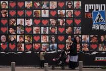 A woman and her children walk past a wall with photographs of hostages who were kidnapped durin ...