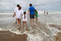 Oscar Salinas, second right, walks his family into the turbulent surf on Tuesday, June 29, 2010 ...