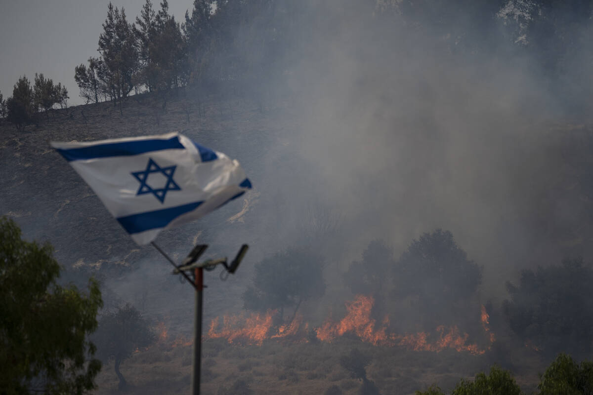 An Israeli flag flutters next to a fire burning in an area near the border with Lebanon, northe ...