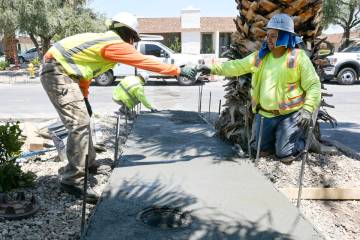 Marco Mendez, left, passes a trowel to Alex Horta from Sunrise Paving while pouring a sidewalk ...