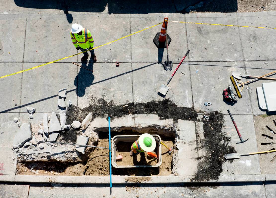 Workers install electric box on the sidewalk at the intersection of Maryland Parkway and Charle ...