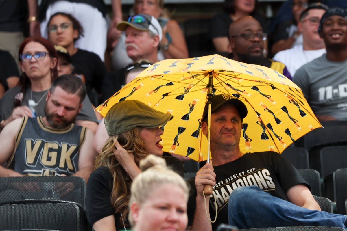 Fans use an umbrella to shield from the rain during the annual Battle for Vegas charity softbal ...
