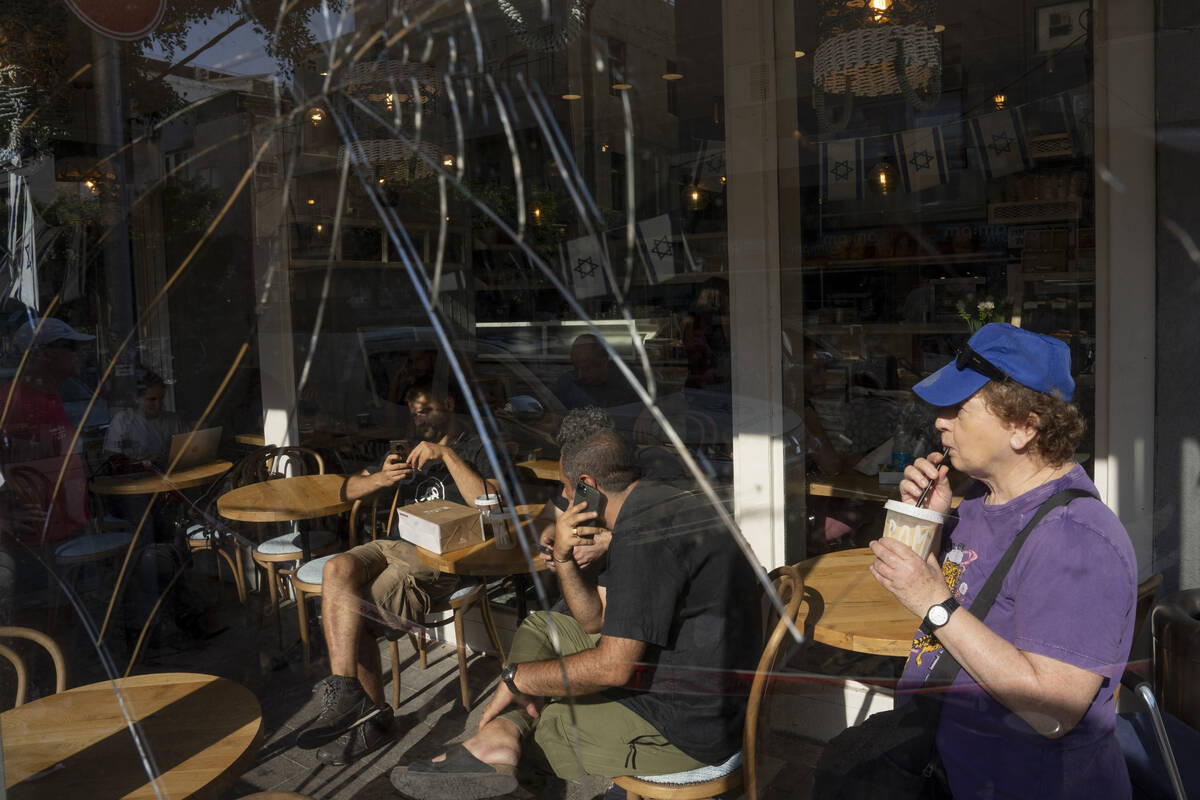 People are seen through a broken coffee shop window next to the scene of an explosive drone att ...