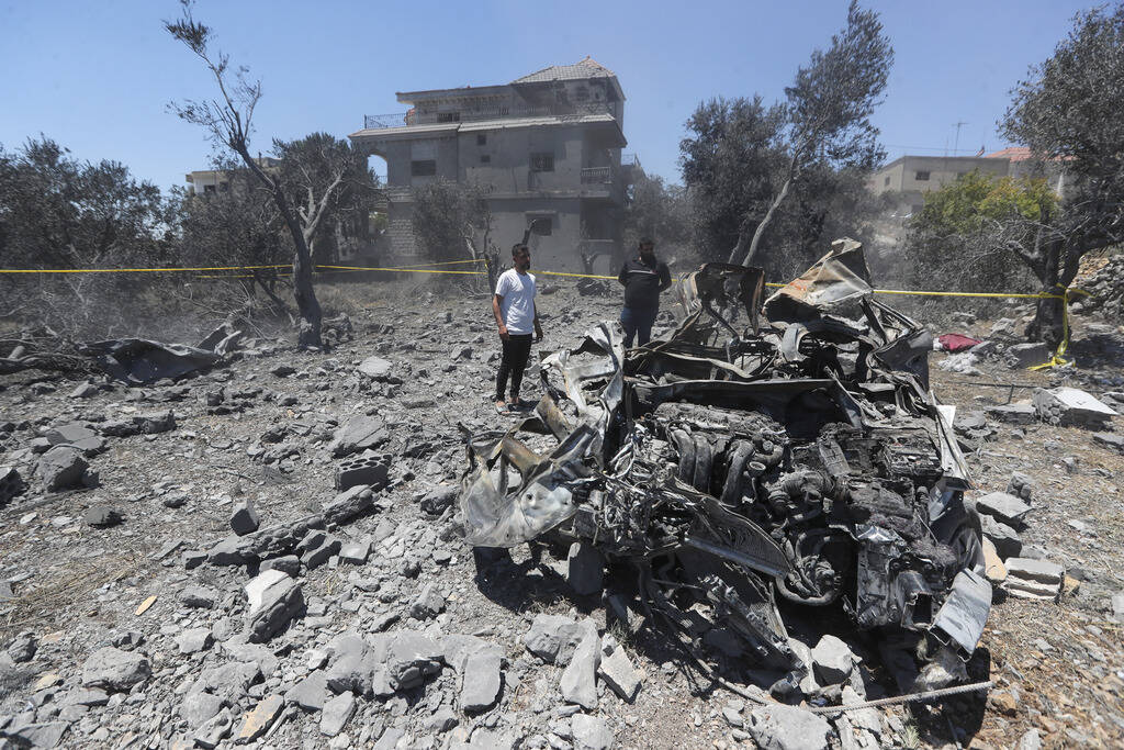 People stand next to a destroyed car that was hit by an Israeli airstrike late Thursday, in the ...