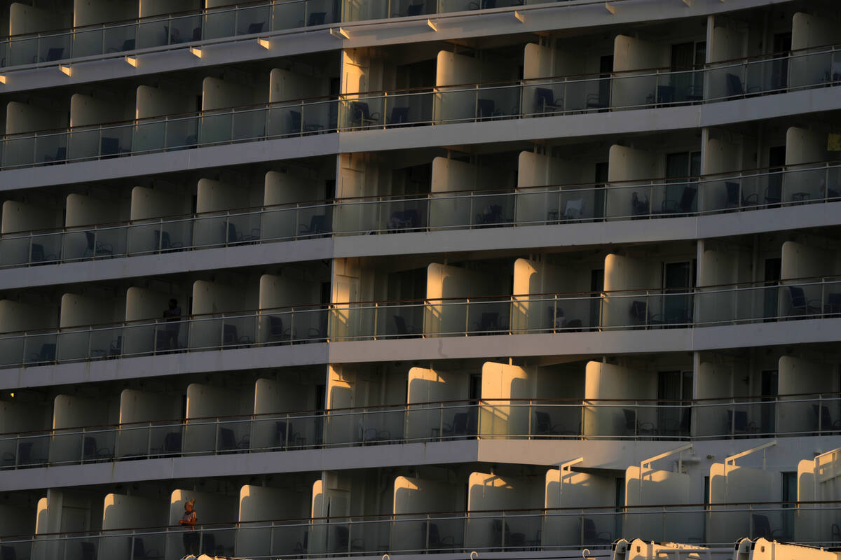A woman, bottom left, stands on the balcony of a cruise ship which is docked at Athens' port ci ...