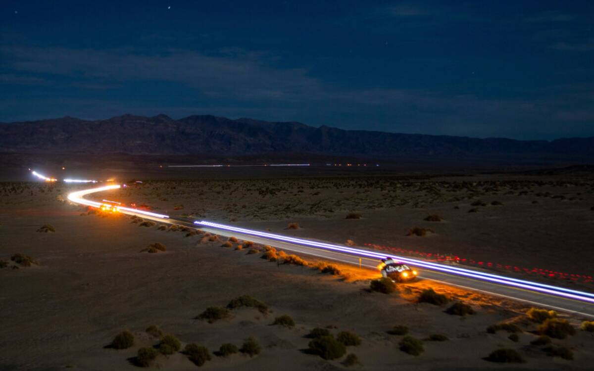 This long exposure image shows the path of runners and their support vehicles under a moon ligh ...