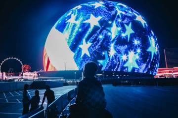 A young child sits on a pair of shoulders as he looks up at the Sphere while fireworks go off i ...