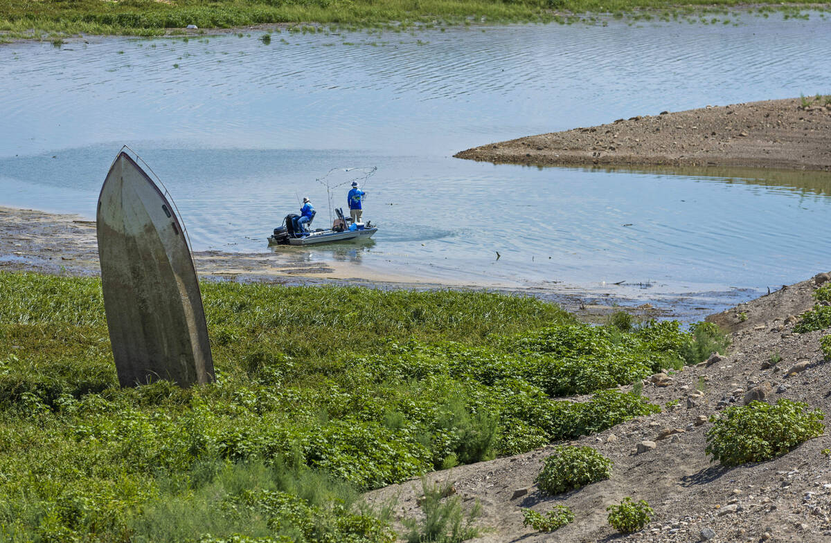 Men fish near a boat sticking up along the shoreline in Government Wash which is now surrounded ...